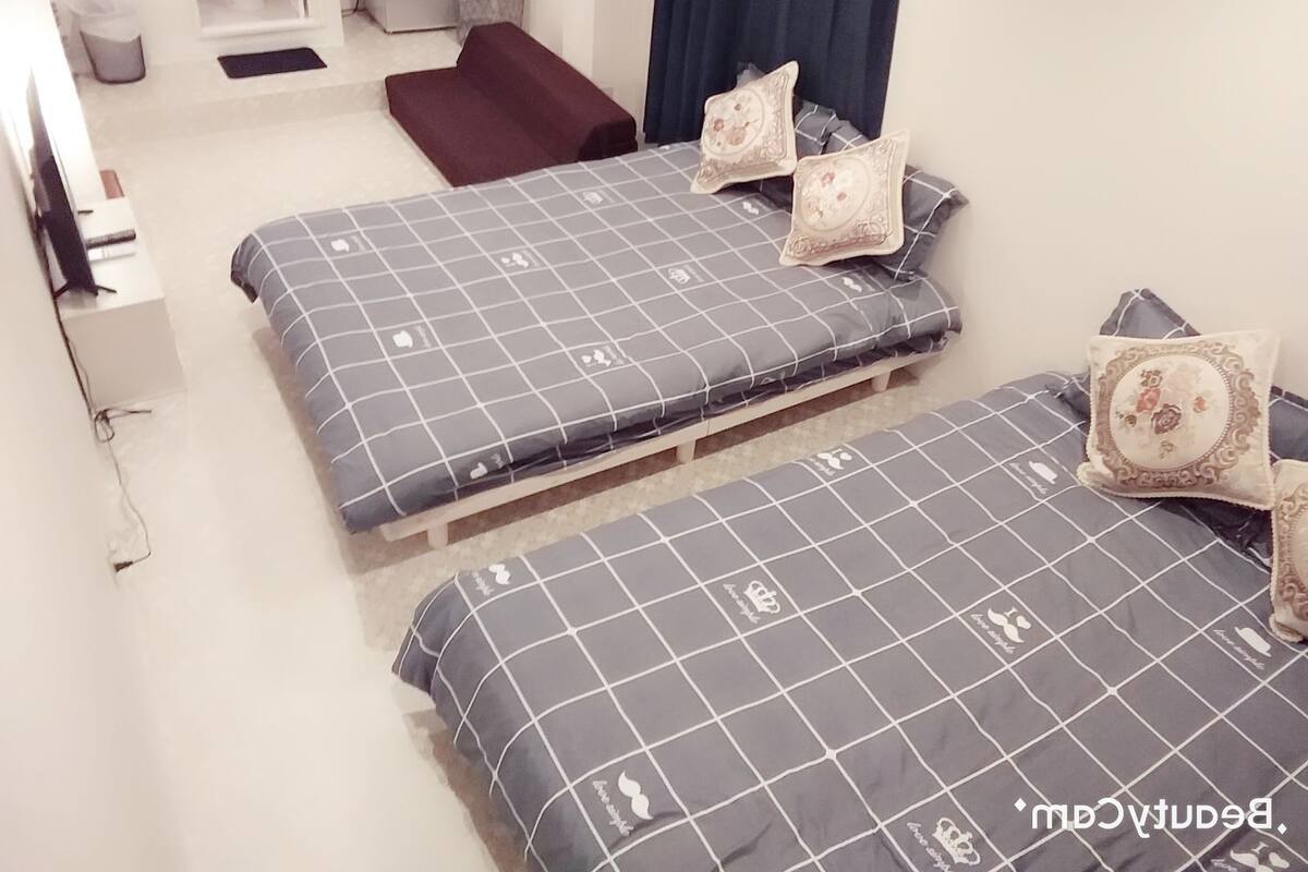 A bedroom with two beds, each with a grey checkered duvet and matching pillows. There is a small round table and a bench in the room.
