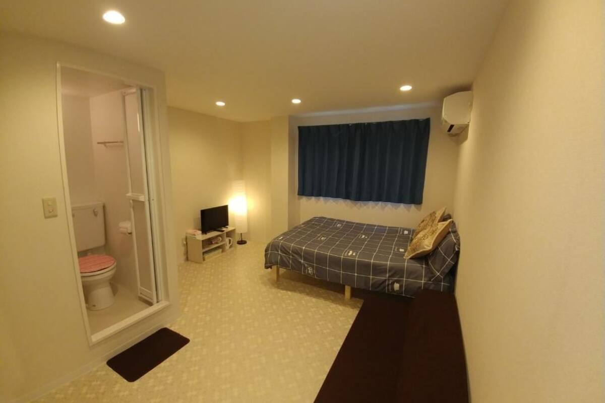 A small, compact room with a bed, a bedside table, a television, and a shower area.