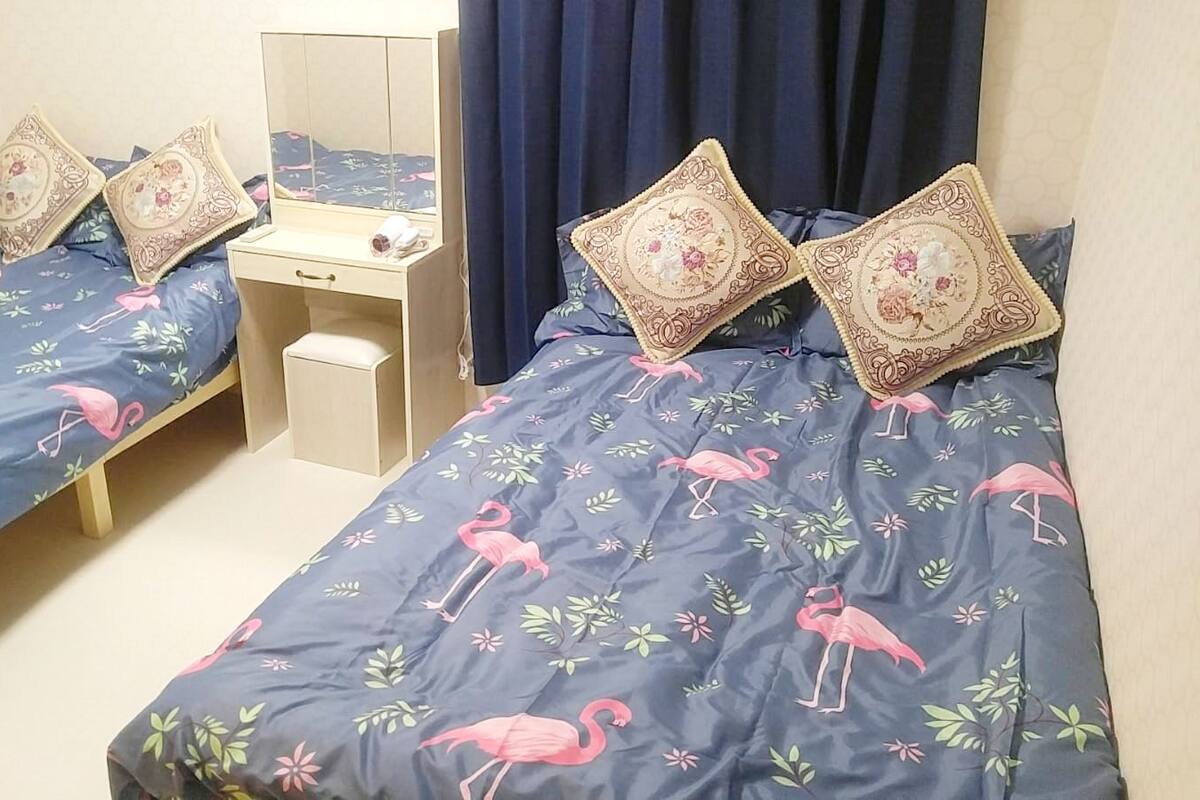 A bedroom with two single beds, each with a floral-patterned duvet and matching pillows. There is a small bedside table with a mirror and a lamp.