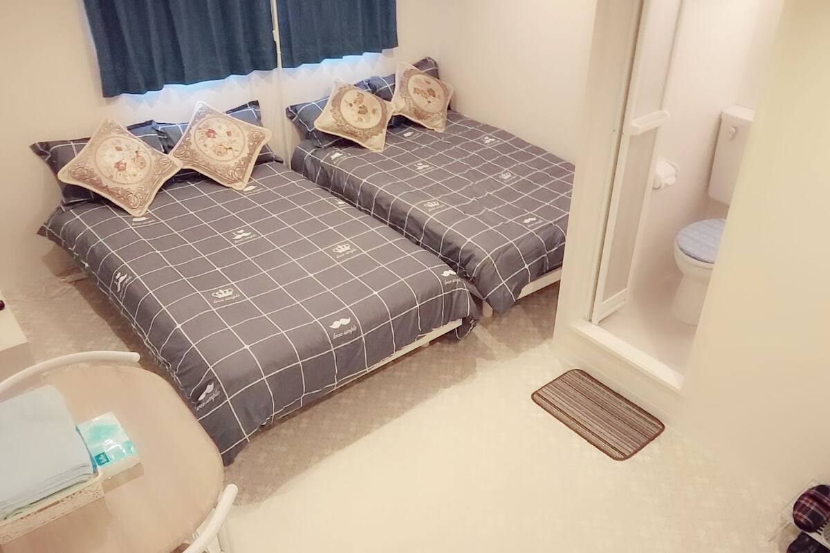 A bedroom with two beds, a small table, and a window with curtains.