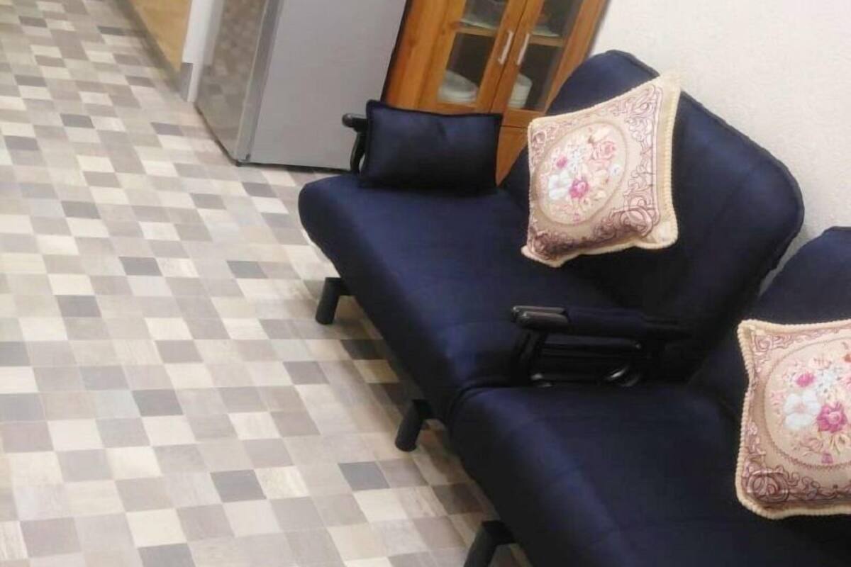 A room with a checkered floor, a sofa with floral cushions, a cabinet, and a microwave.