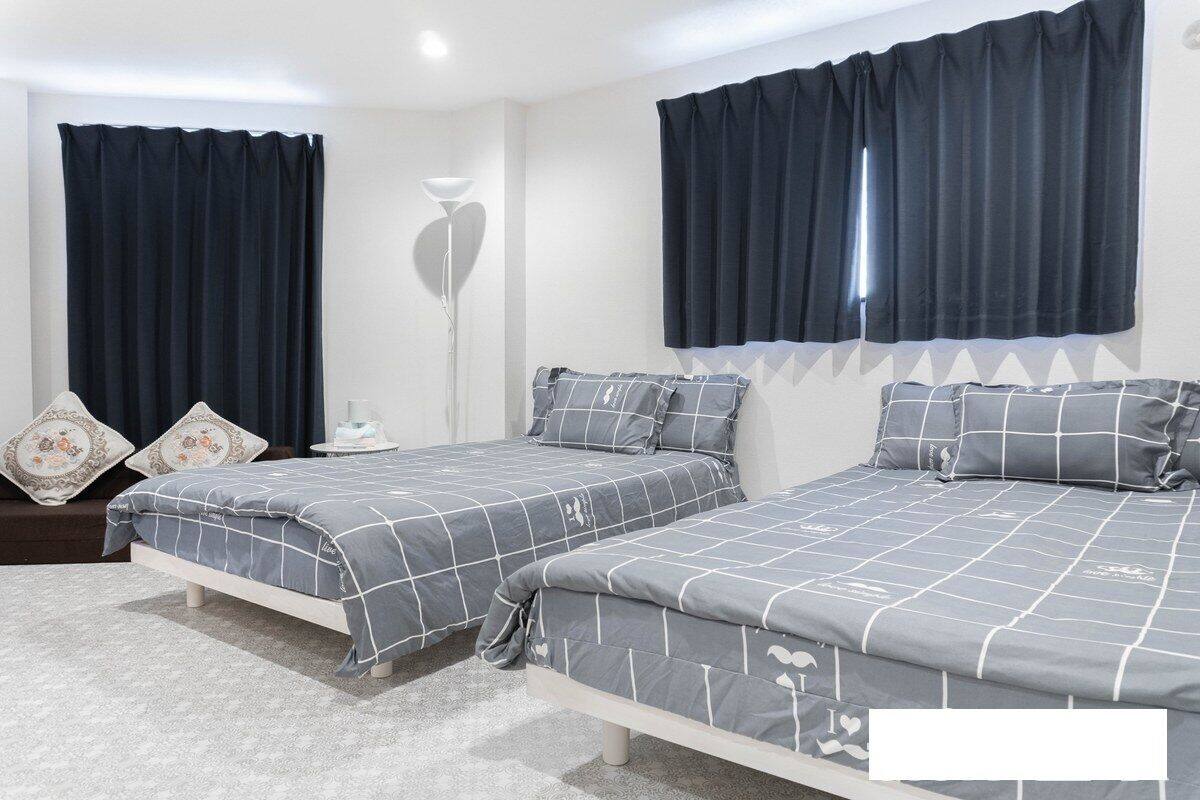 A bedroom with two beds, dark curtains, a bedside table, and a floor lamp.