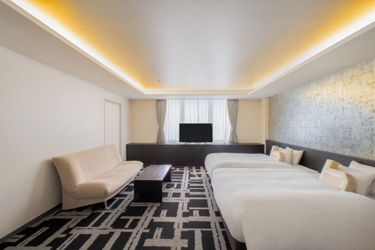 Een hotelkamer met een bank, twee bedden, een televisie en een kamerbreed tapijt met dessin.