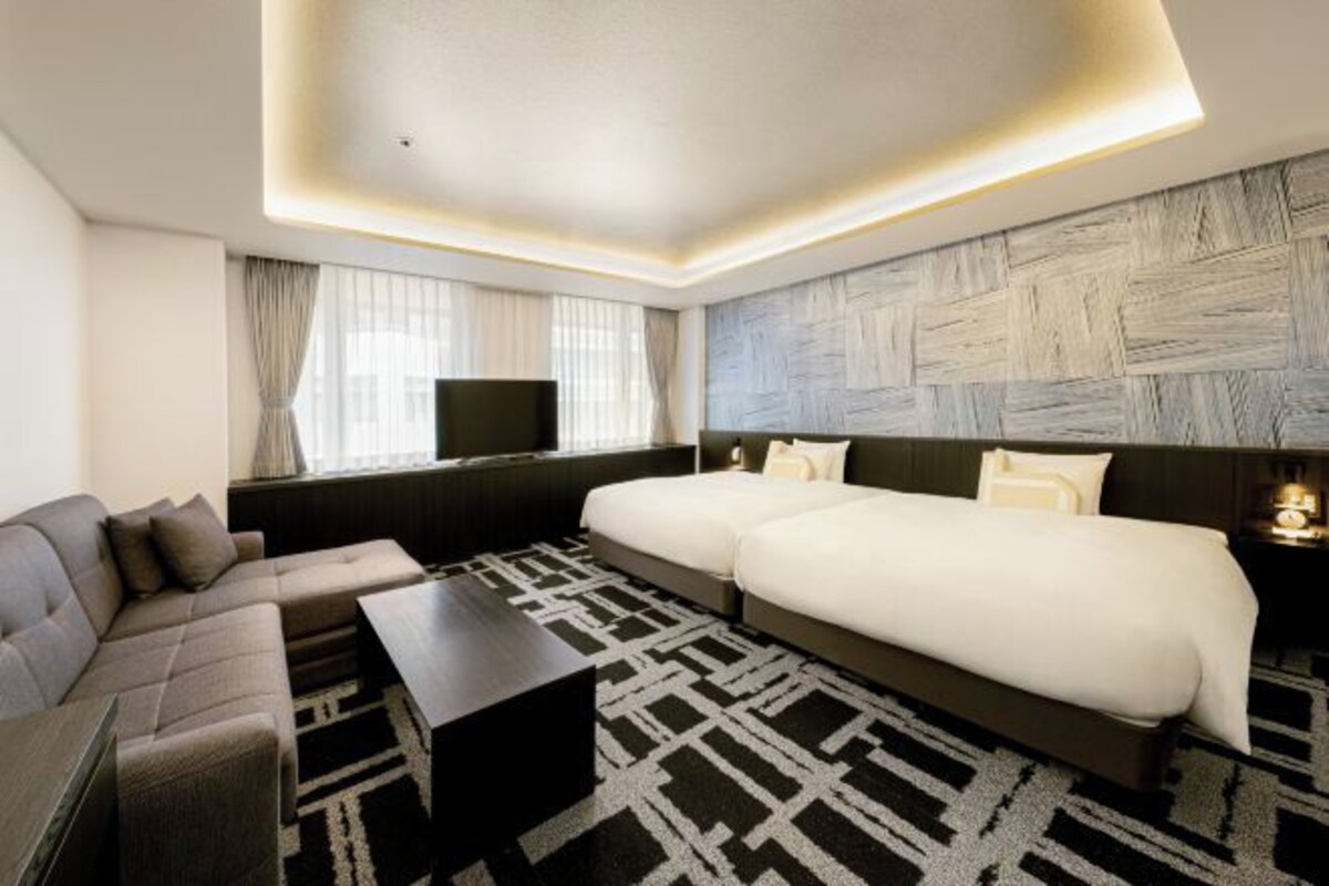 Ein modernes Hotelzimmer mit einer Eckcouch, einem großen Bett und einem Flachbildfernseher.