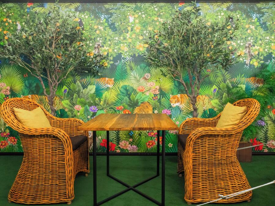 A room with wicker furniture, a wooden table, and a mural of a jungle scene.
