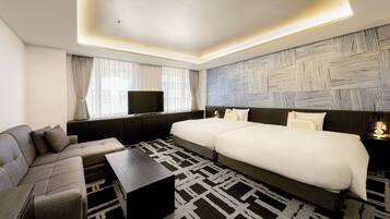 A modern hotel room with a sofa, a large bed, a flat-screen TV, and a patterned rug.