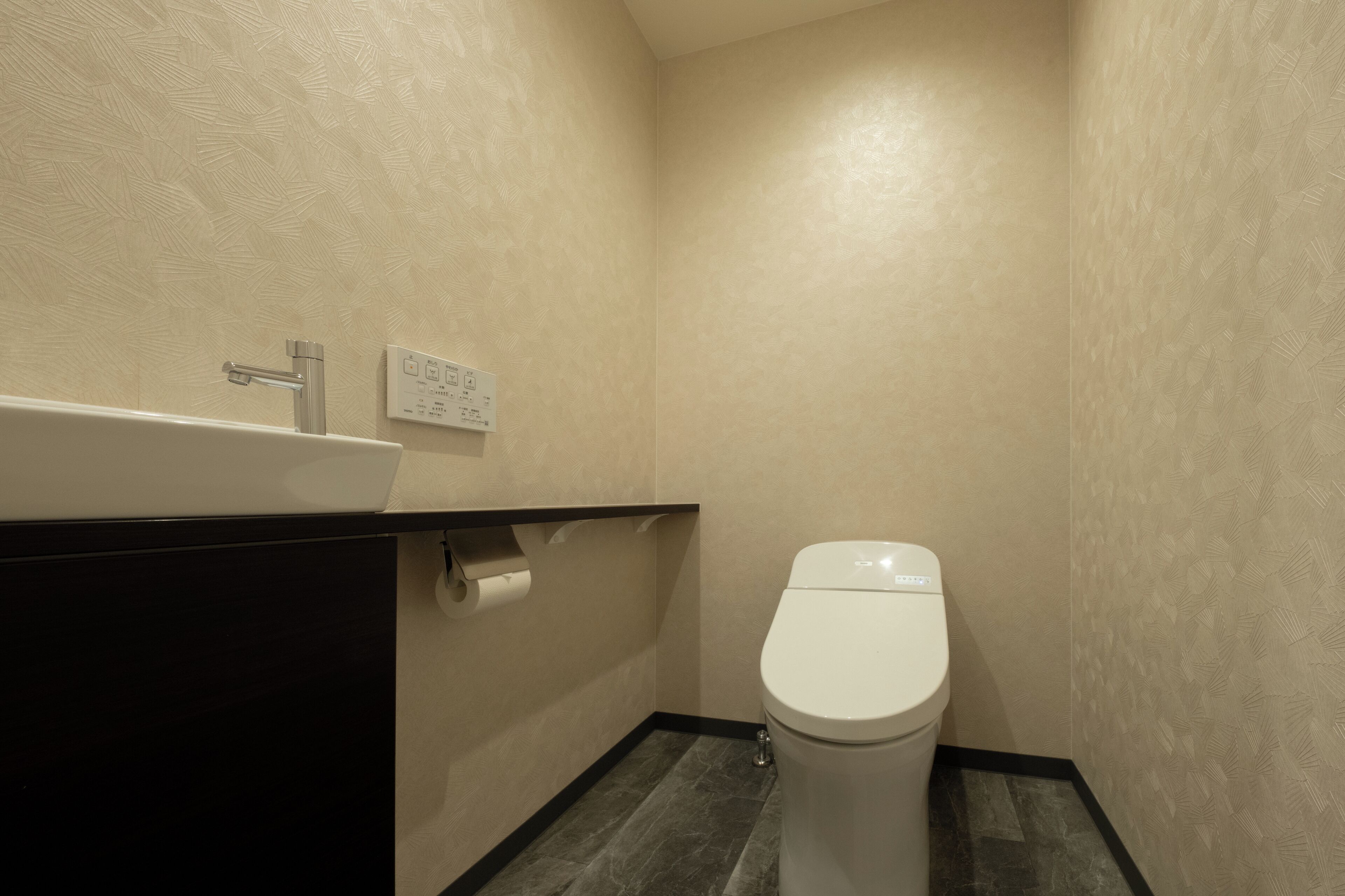 Un baño pequeño y moderno con inodoro blanco, tocador negro y grifo empotrado en la pared.