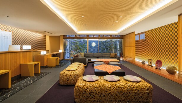 Un hall d’hôtel moderne avec un motif à carreaux sur le mur, un comptoir d’accueil en bois, un espace salon confortable et de grandes fenêtres offrant une vue sur la verdure.