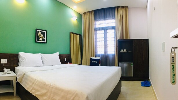 A hotel room with a large bed, a nightstand with a phone, a framed picture on the wall, a wardrobe, and a window with curtains. - Spring Hotel (Ho Chi Minh City)