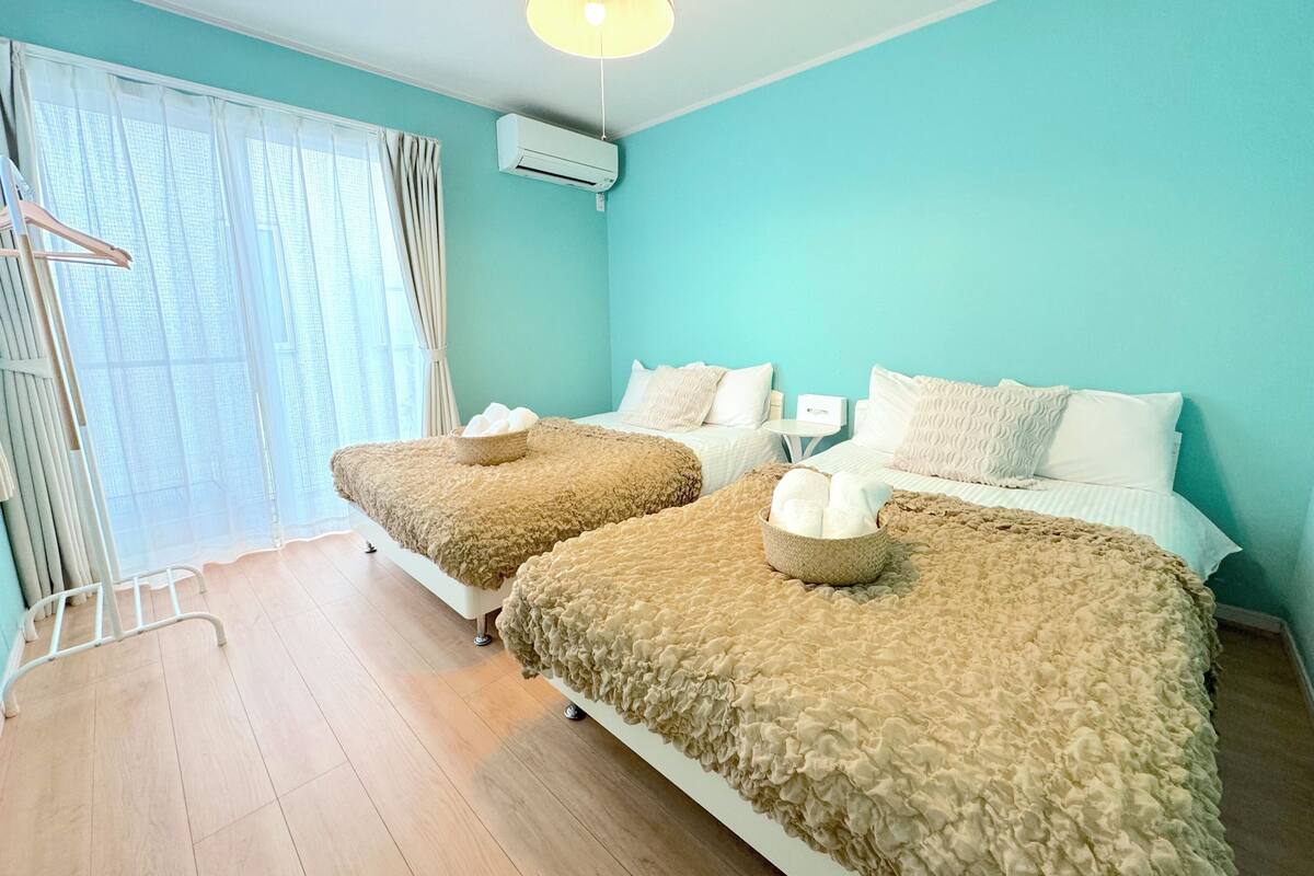 Une chambre d’hôtel avec deux lits, une fenêtre avec des rideaux légers, un luminaire au plafond et un appareil de climatisation.