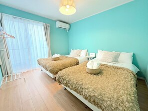 Ein Hotelzimmer mit zwei Betten, einem Fenster mit durchsichtigen Vorhängen, einer Deckenleuchte und einer Klimaanlage.