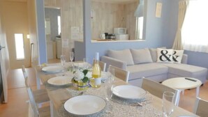 A dining area with a table set for four, a sofa, and a kitchen in the background. - Grandioso Okinawa Villa Onna 2 (Onna)