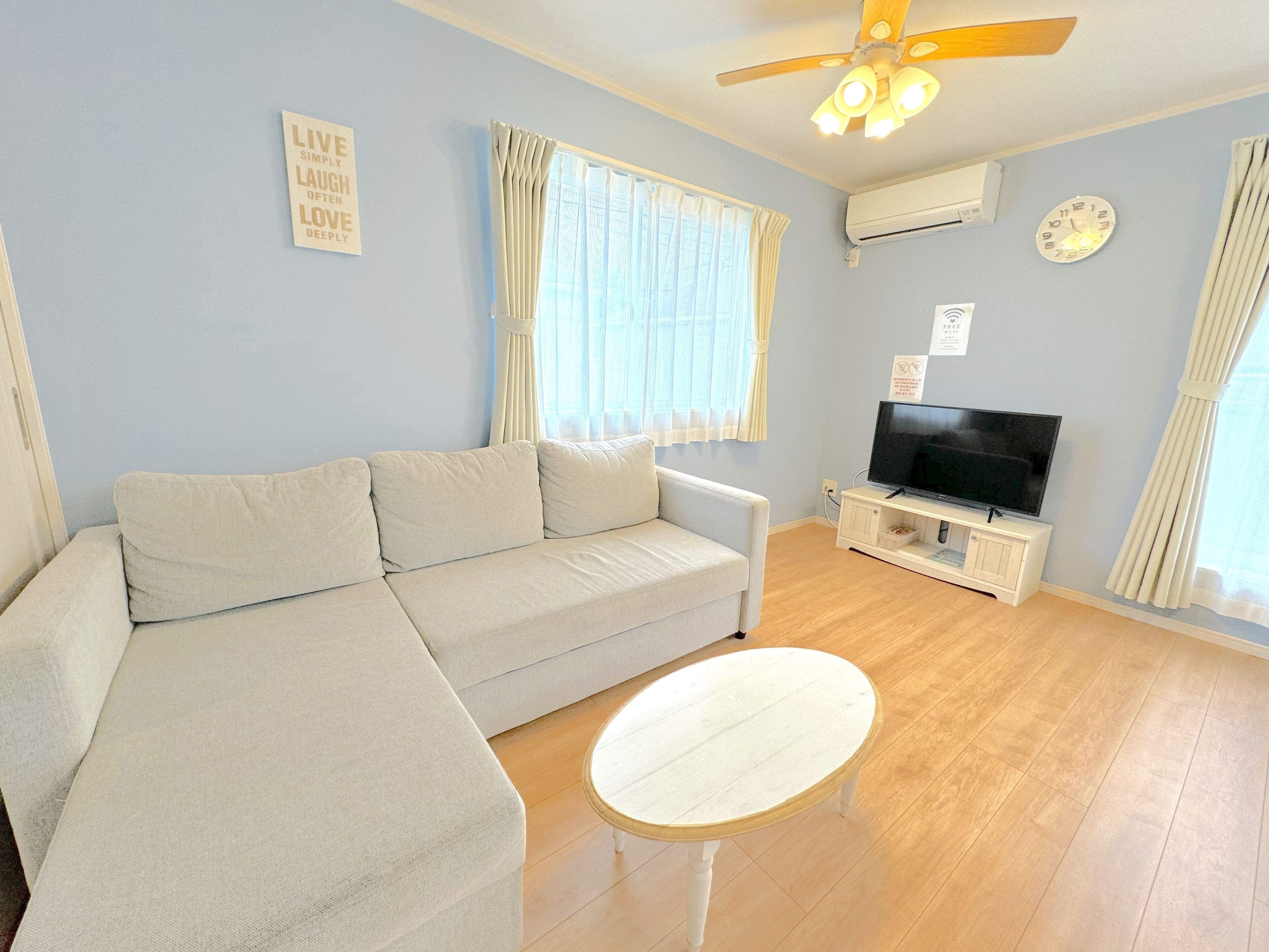 A living room with a sofa, a small table, a ceiling fan, a TV, and a clock on the wall.
