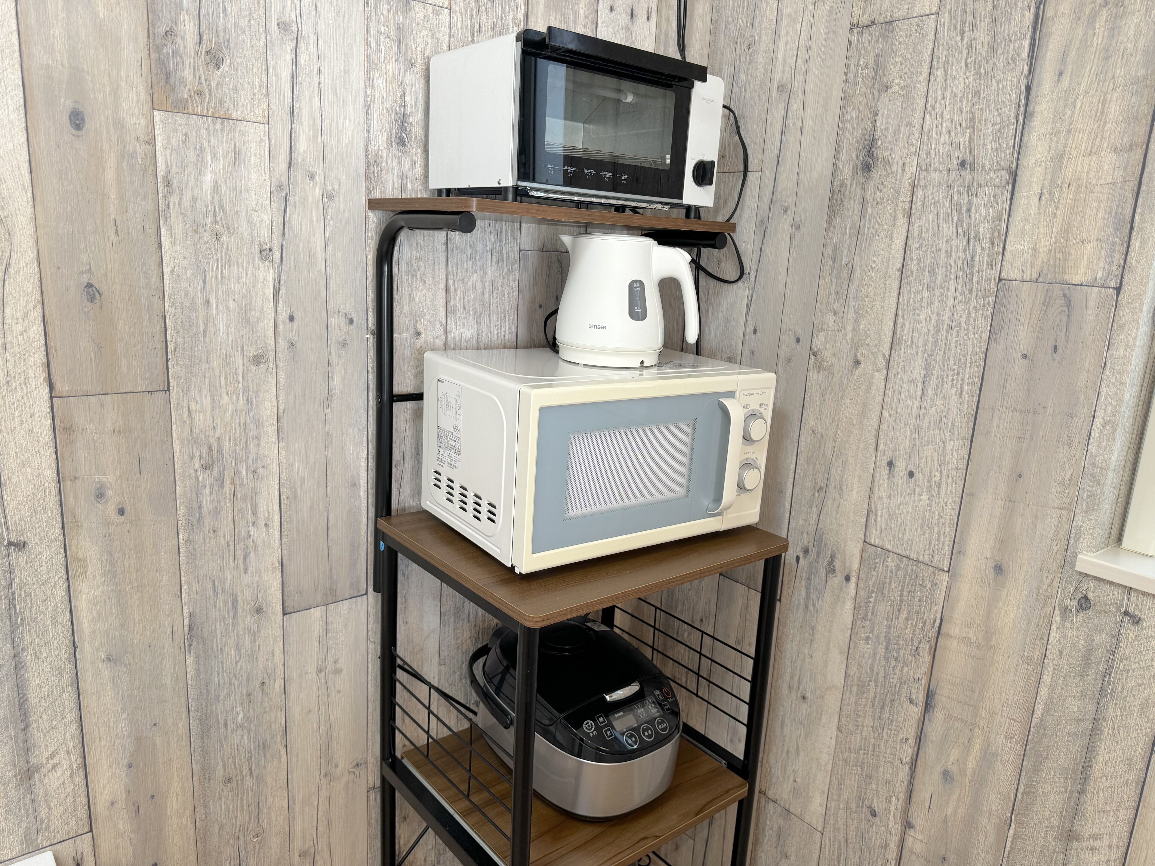 A kitchen with a microwave, kettle, and rice cooker on a wooden shelf unit.