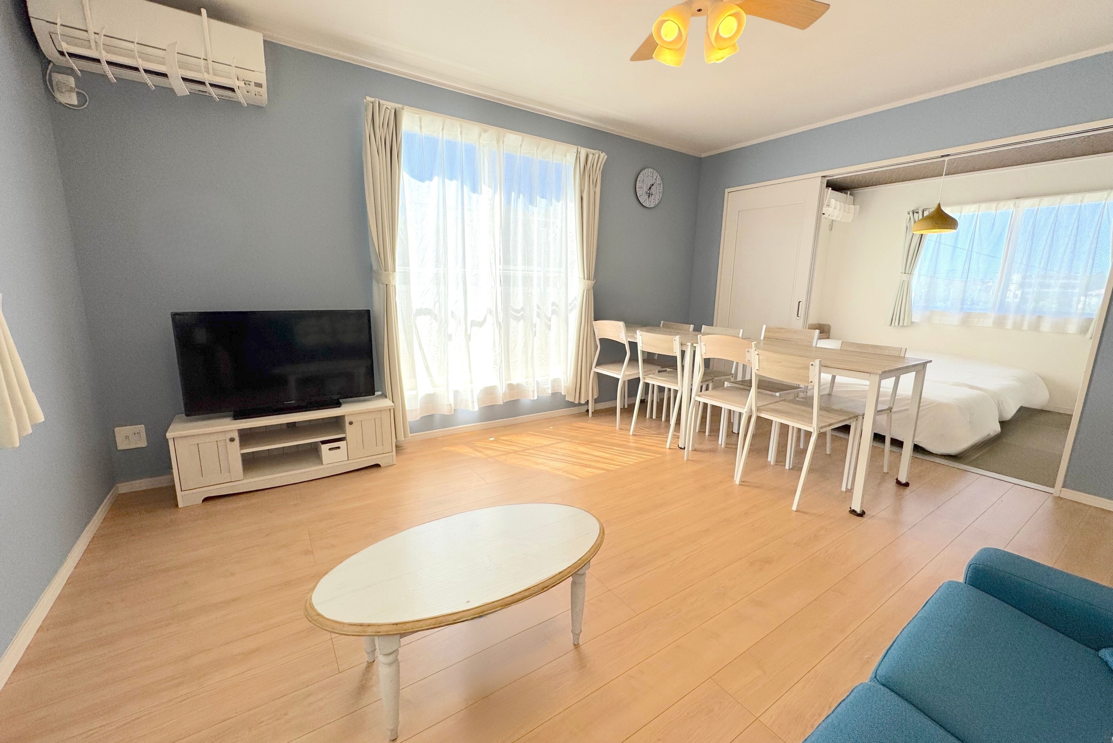 A living room with a television, a dining table with chairs, a sofa, and a ceiling fan.