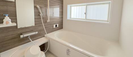 A modern bathroom with a large bathtub, a shower, a vanity with a mirror, and a window providing natural light.