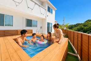 A swimming pool with wooden deck and a white building in the background. - Grandioso Okinawa Villa Onna 2 (Onna)
