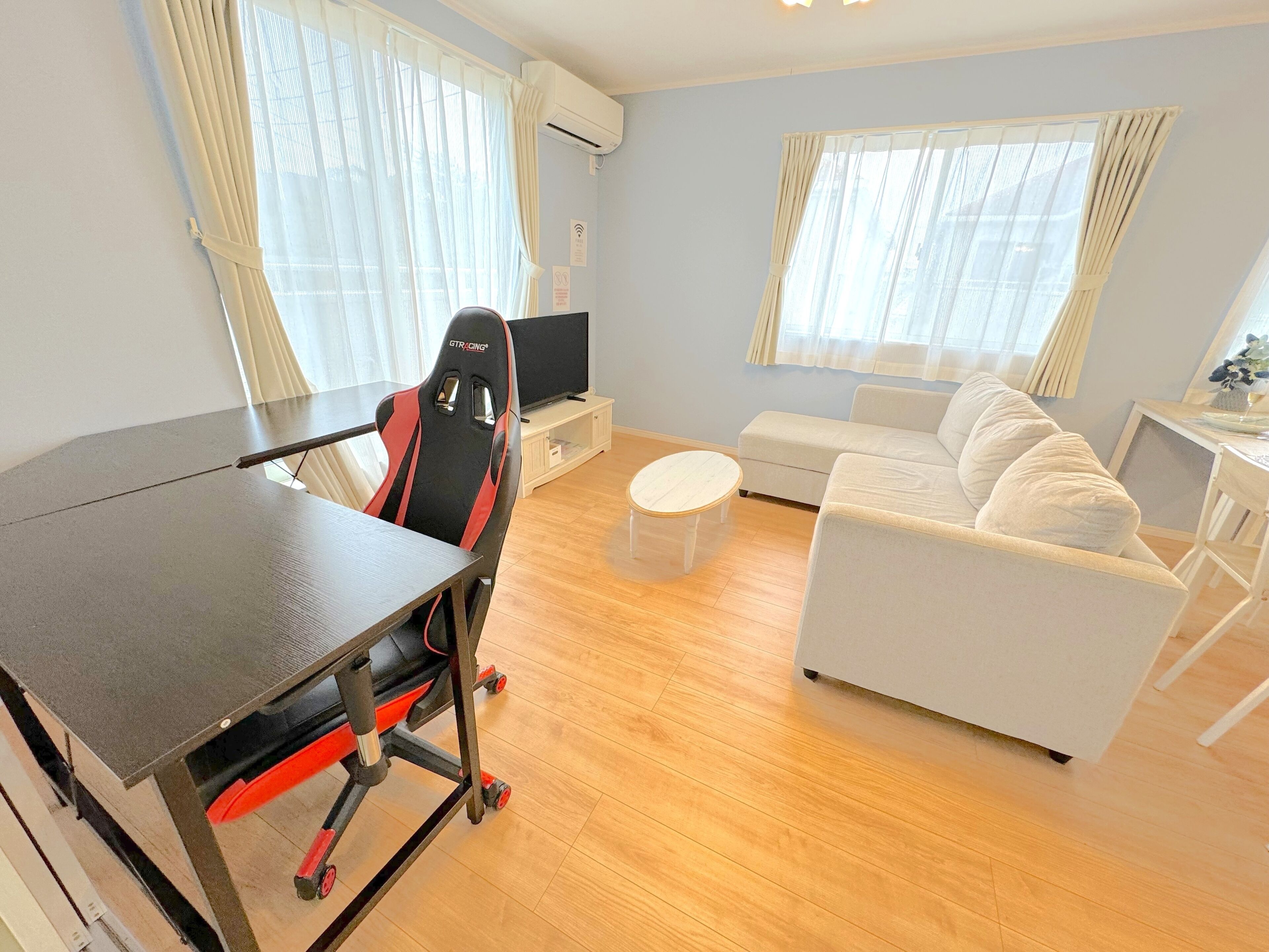 A modern living room with a gaming chair, a sofa, a small round table, and a TV.