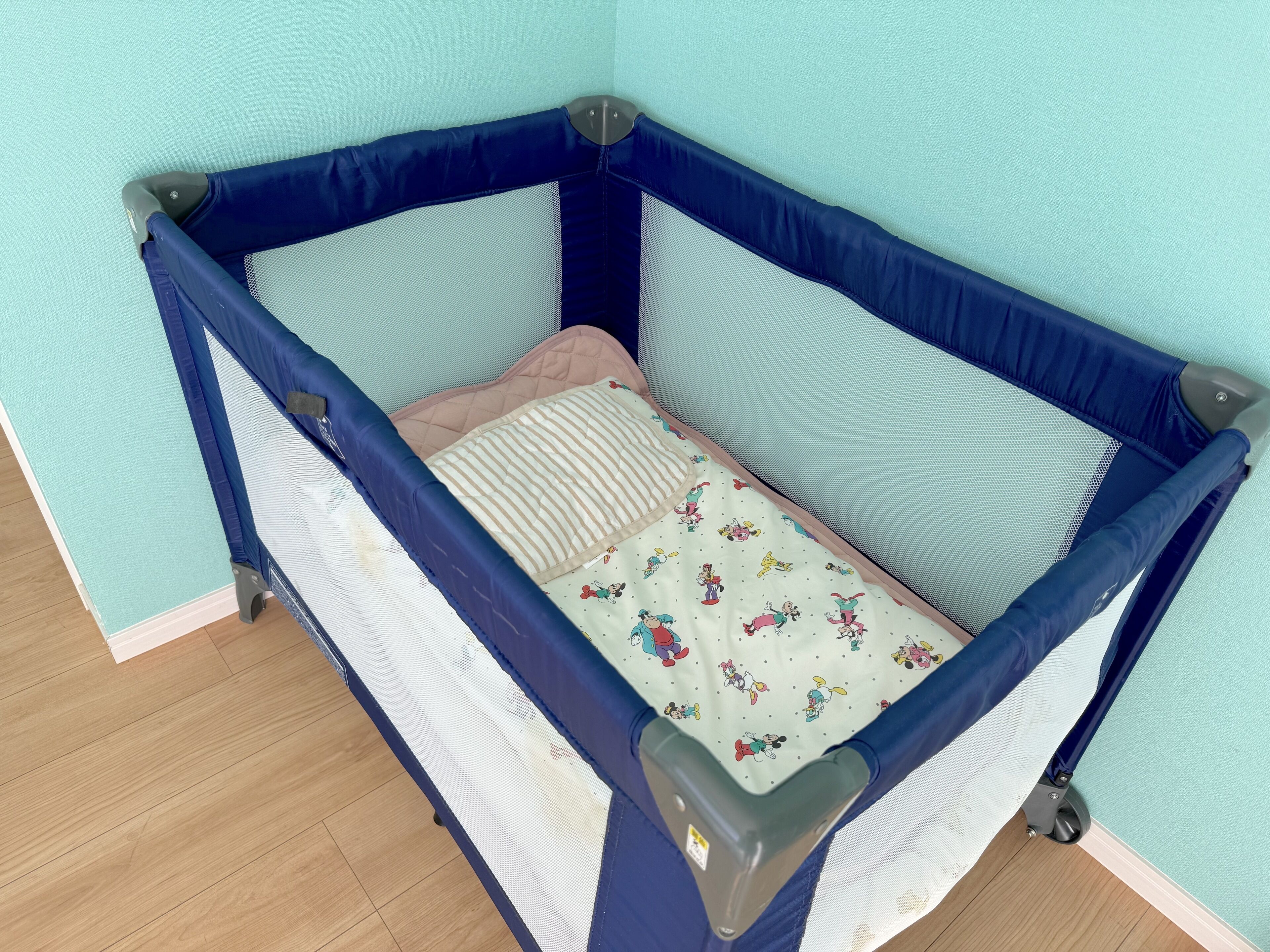 A baby crib with a blue frame, a quilted mattress, and a cushion.