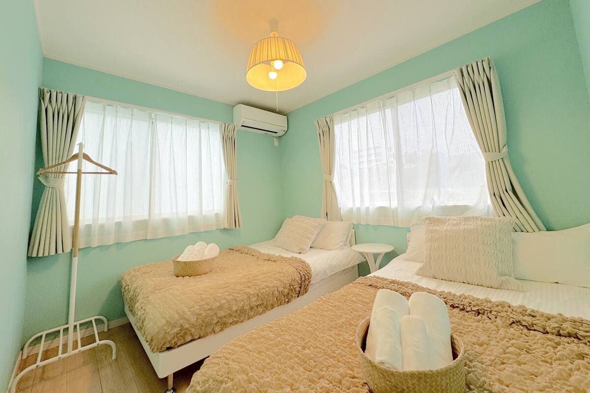 Une chambre avec deux lits, une table de chevet, une lampe et une fenêtre avec des rideaux.