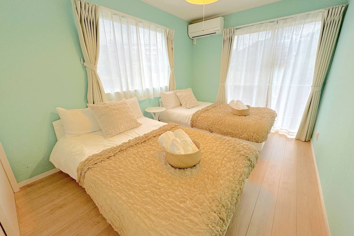 Une chambre d’hôtel avec deux lits, chacun recouvert d’une couverture beige moelleuse et agrémenté d’oreillers, une petite table ronde et un ventilateur de plafond.