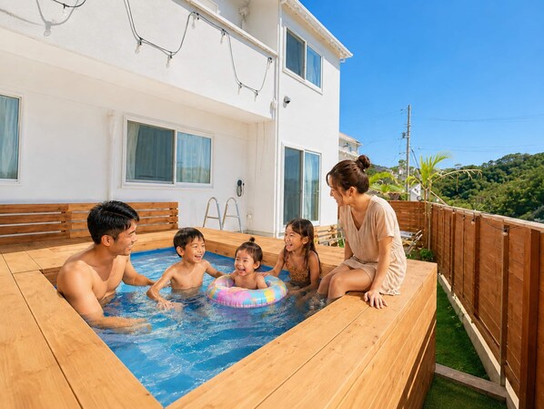 Zona de piscina con un muelle de madera, un edificio blanco con ventanas y vistas a zonas verdes al fondo.