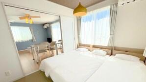A hotel room with a large bed, a ceiling fan, a dining area with a table and chairs, and a view of the outdoors through the window. - Grandioso Okinawa Villa Onna 2 (Onna)