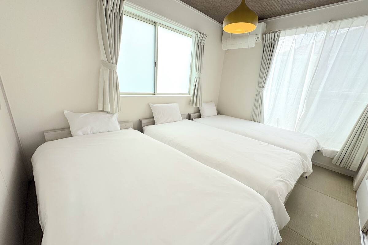 Une chambre d’hôtel avec deux lits, une fenêtre avec des rideaux, un luminaire au plafond et un climatiseur fixé au mur.