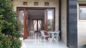 A modern building entrance with glass doors, a small patio with two white chairs, and a potted plant to the left. - Villa Uma Dangin (Ubud)