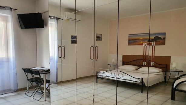 A bedroom with a bed, a desk, chairs, a TV, and a painting on the wall. - B&B Pizzomunno e Cristalda Rooms (Vieste)