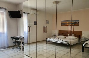 A bedroom with a bed, a desk, chairs, a TV, and a painting on the wall. - B&B Pizzomunno e Cristalda Rooms (Vieste)