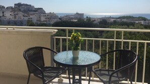 A balcony with a round glass table and two chairs, overlooking a coastal town with buildings and the sea. - B&B Pizzomunno e Cristalda Rooms (Vieste)