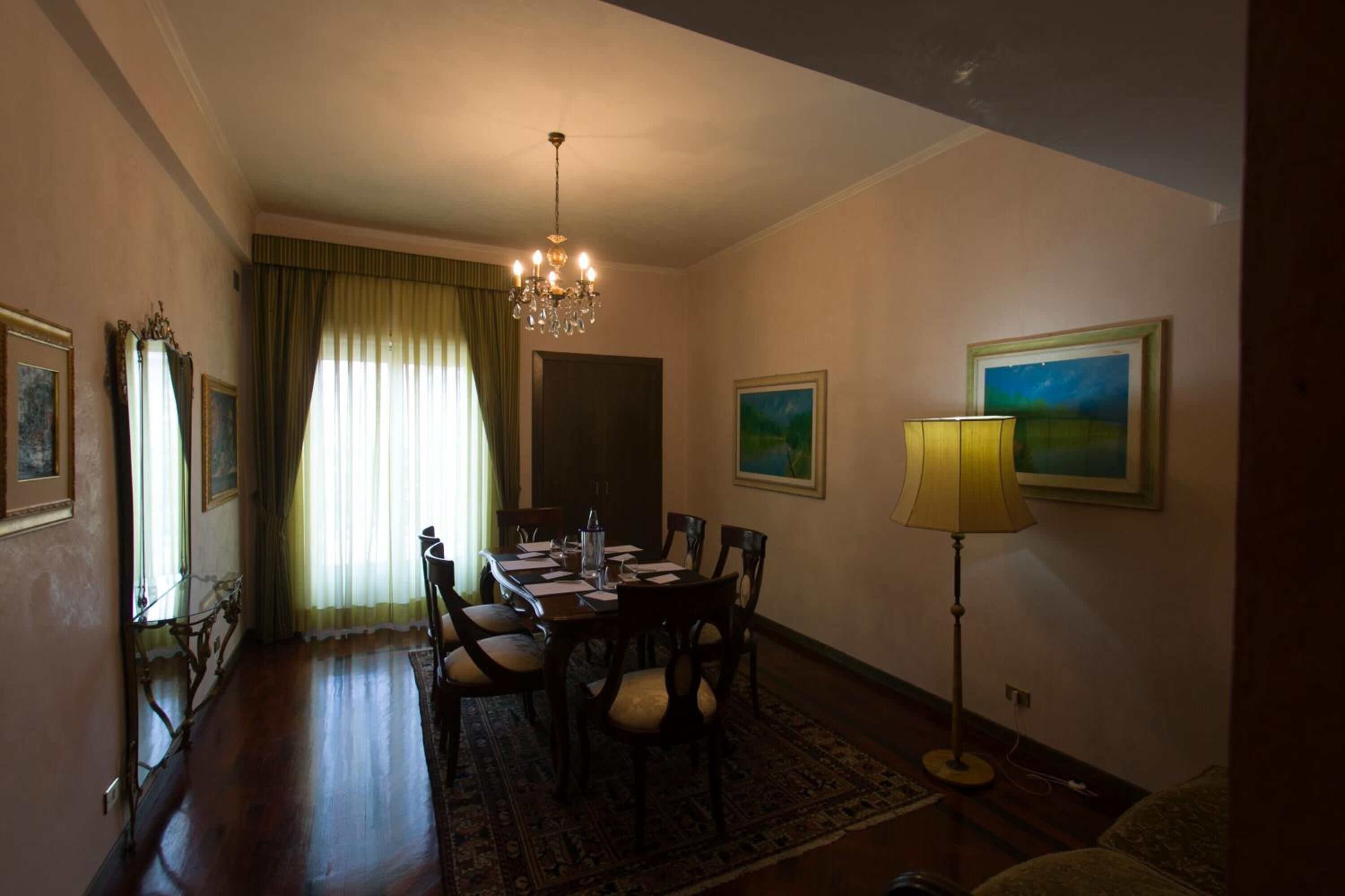 A dining room with a chandelier, dining table, chairs, and a lamp.