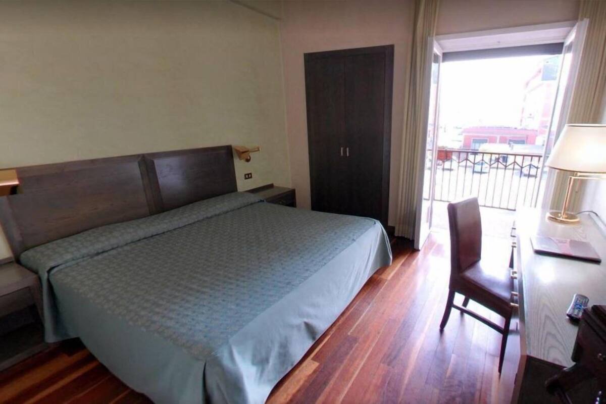 Ein Hotelzimmer mit Bett, Schreibtisch mit Stuhl, Kleiderschrank und einem Balkon mit Geländer.