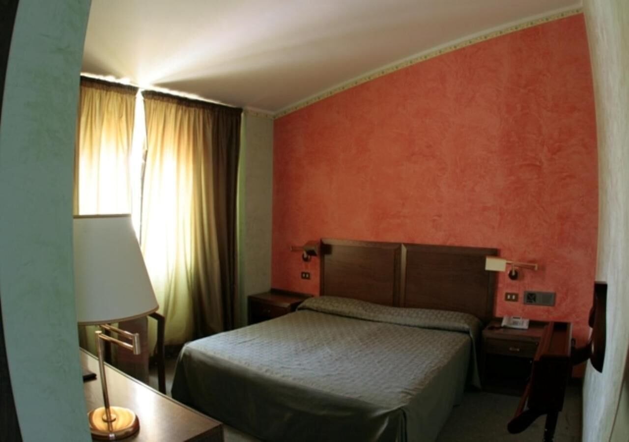 A hotel room with a single bed, a nightstand, a lamp, and a window with curtains.