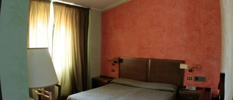 A hotel room with a single bed, a nightstand, a lamp, and a window with curtains.