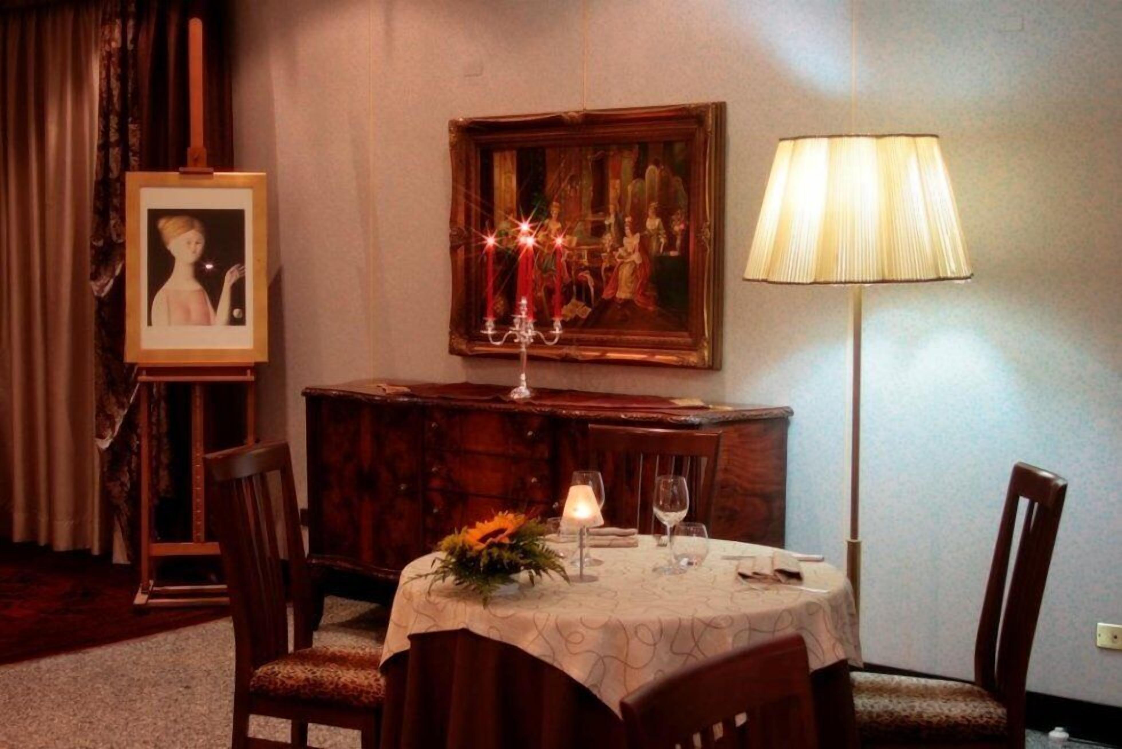 A dining area with a round table, chairs, a painting, a lamp, and a candle.