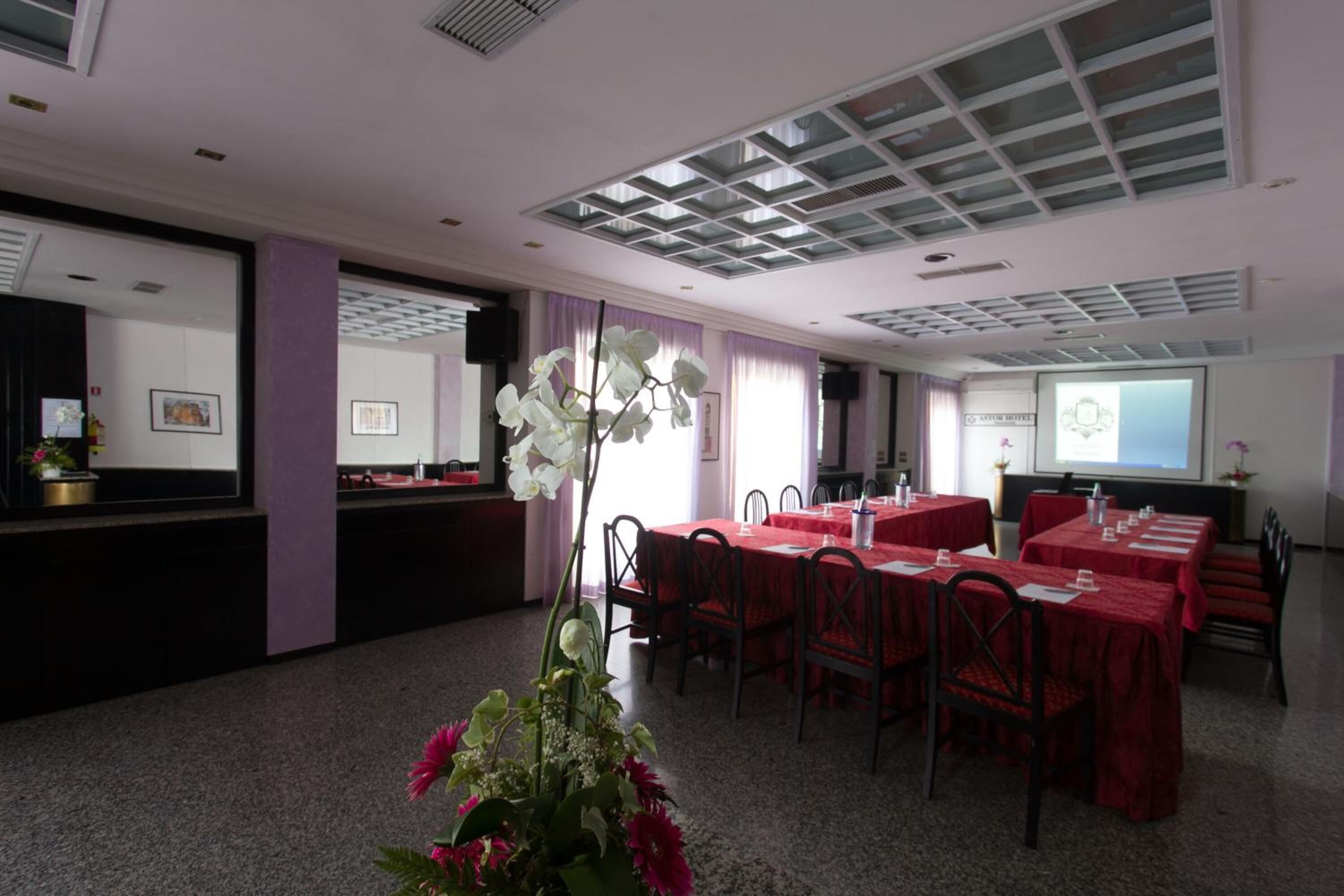 A conference room with tables and chairs, a projector screen, and a floral arrangement.