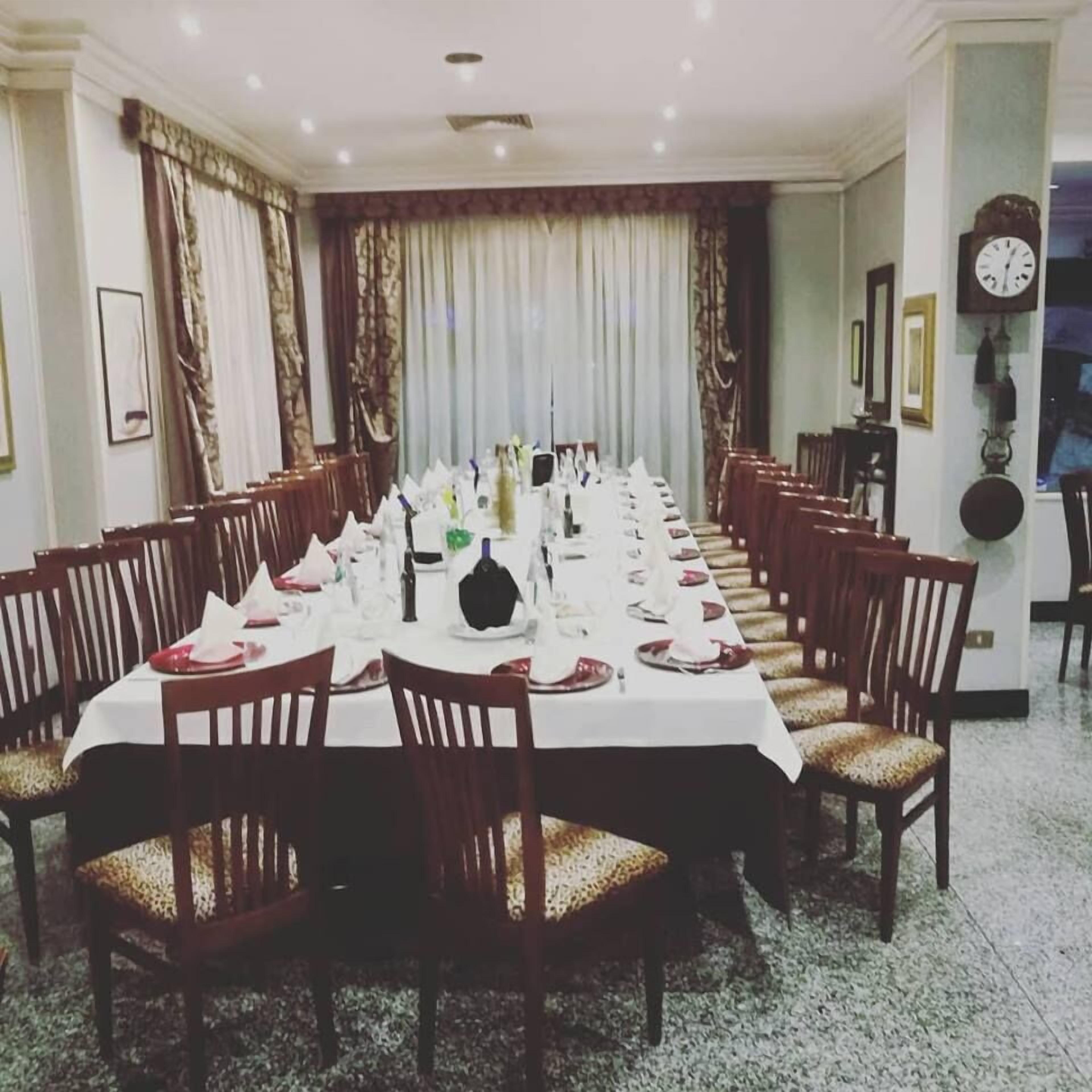 A formal dining room with a long table set for a meal, surrounded by wooden chairs with cushioned seats.