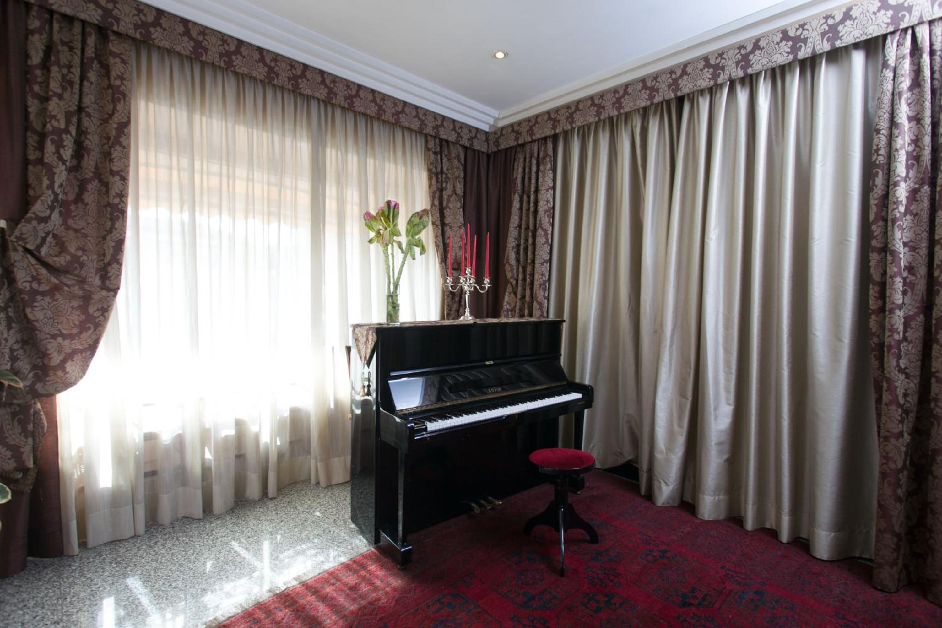 A room with a grand piano, a red carpet, and patterned curtains.