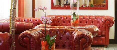 Un sofá de cuero rojo con una mesa de centro de vidrio, una planta de bambú alta y un jarrón con orquídeas rosadas.