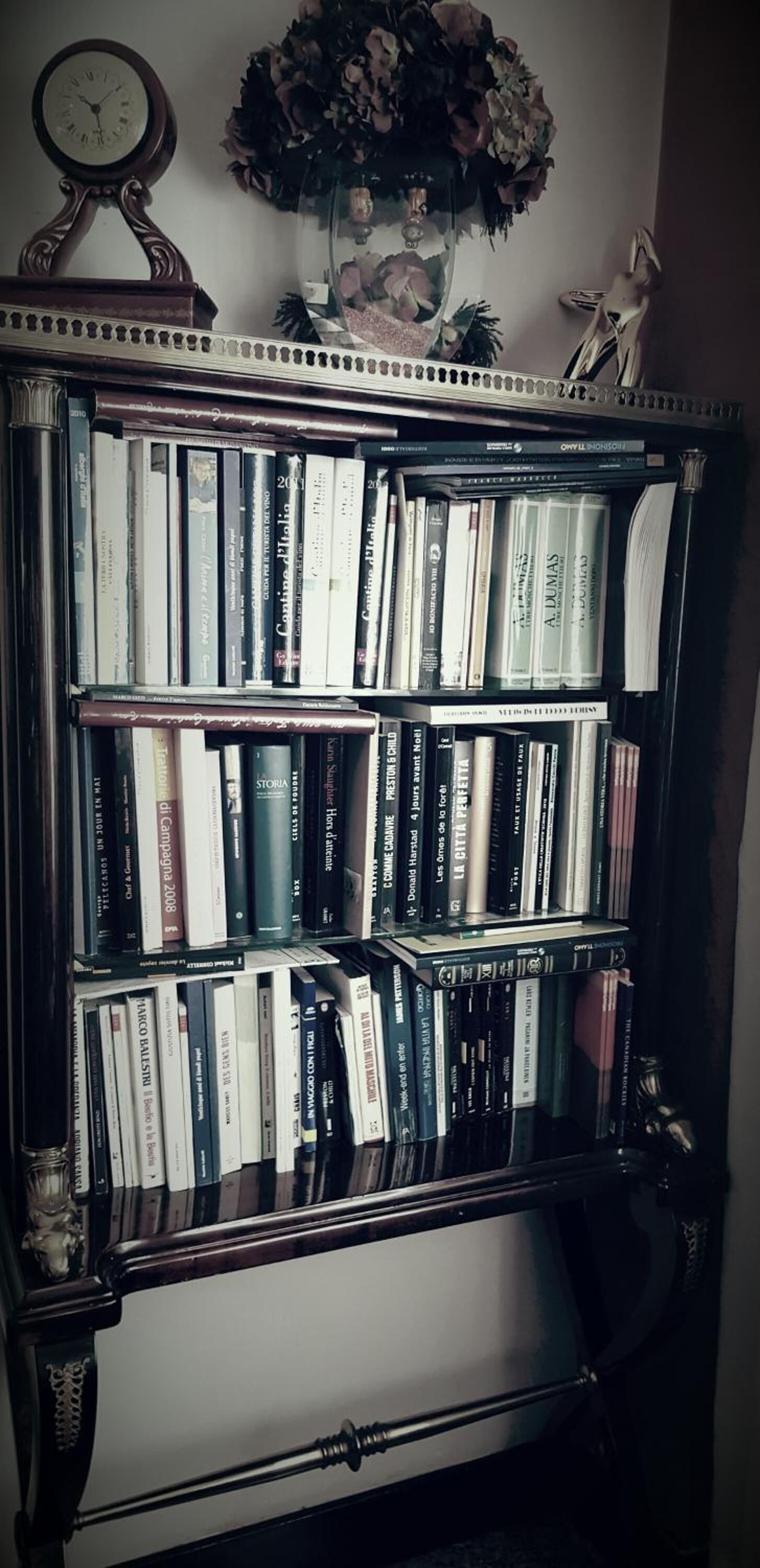 Una libreria piena di libri, un orologio e un'asse di fiori appesi al muro.