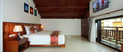 A hotel room with a wooden ceiling, a bed with a white and red bedspread, a nightstand with a lamp, and a TV mounted on the wall.
