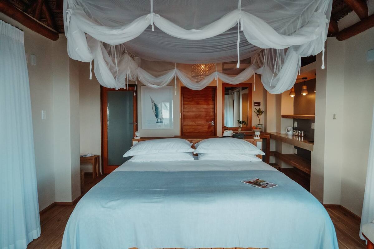 A bedroom with a large bed, a wooden headboard, a bedside table with a lamp, and a wall-mounted artwork.