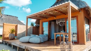 Una cabaña frente al mar con terraza de madera, comedor y techo de paja.