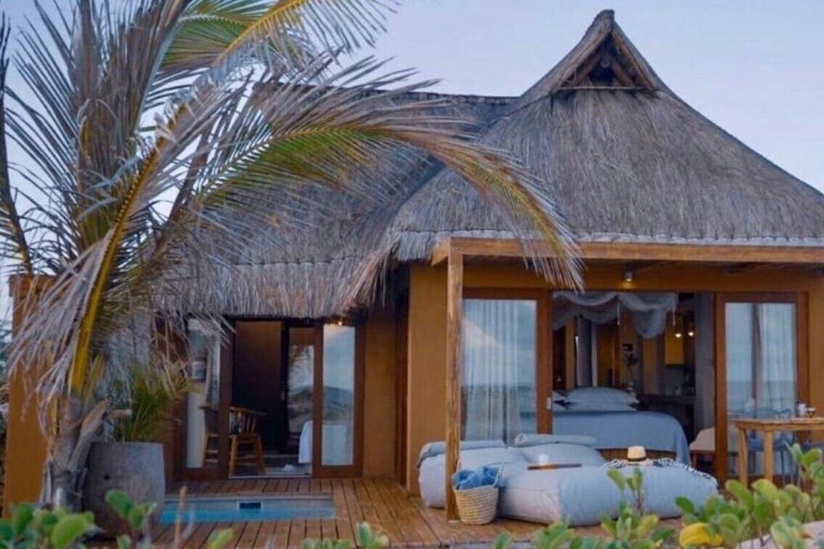 A thatched-roof bungalow with a wooden deck, a pool, and a bedroom with a bed and seating area.