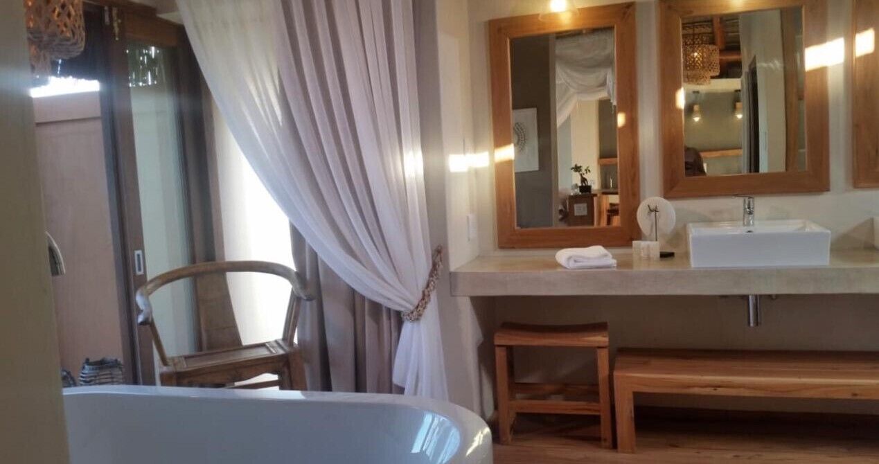 Un bagno con una panca in legno, uno specchio grande e un lavandino bianco.