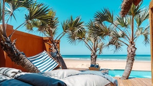 Un dormitorio frente a la playa con una hamaca, palmeras y vista al océano.