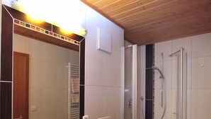 A modern bathroom with a wooden ceiling, a large mirror, a sink, a toilet, and a glass-enclosed shower. - Pension St. Georg Mit Moststüberl (Bad Griesbach im Rottal)