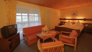 A hotel room with a wooden ceiling, a bed with pillows, a sofa, a small table with a bottle and glasses, and a television on a wooden cabinet. - Pension St. Georg Mit Moststüberl (Bad Griesbach im Rottal)